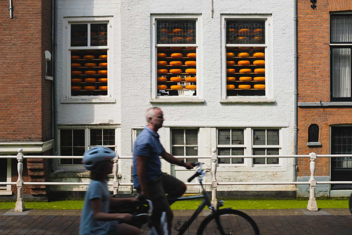 A father and daughter bike past a cheese shop